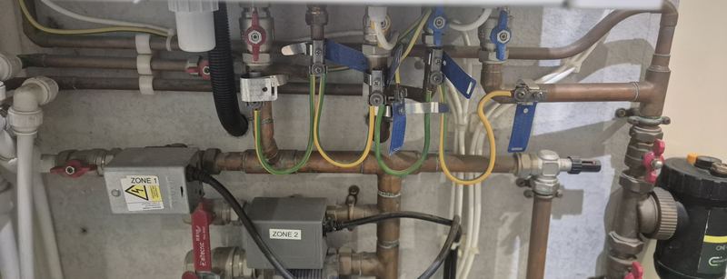 New earth bonding clamps fitted to gas and water pipework under a boiler